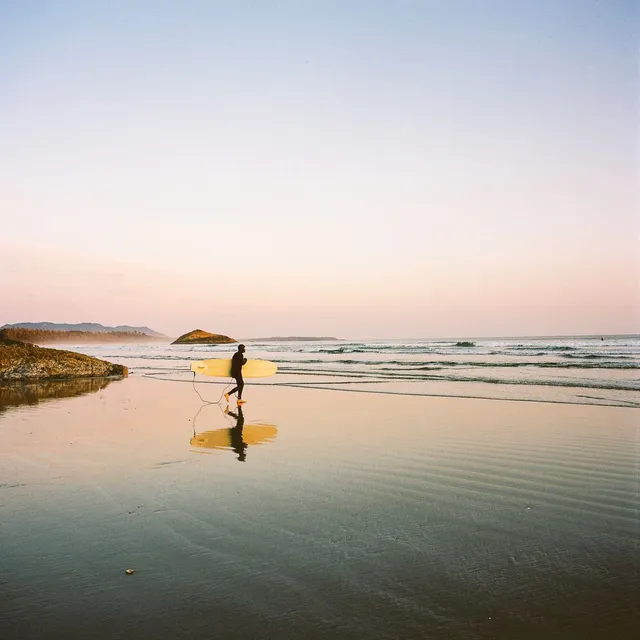 Surfer walking up a reflective beach carrying a yellow board