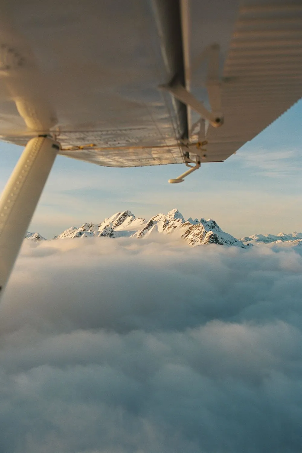 Snowy peaks above clouds under a plane wing