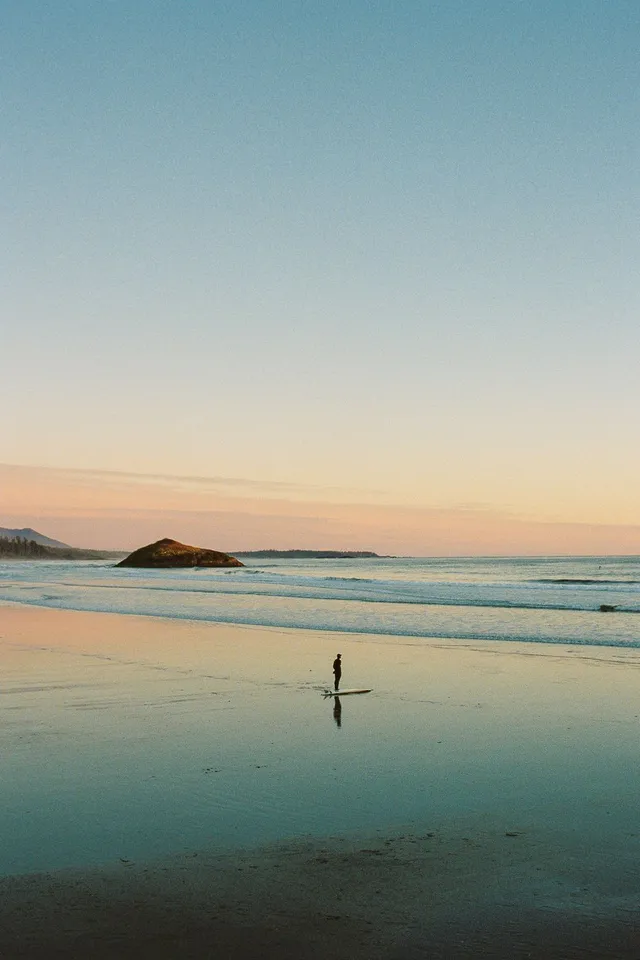 Lone surfer on a glassy beach at dusk with a small island behind