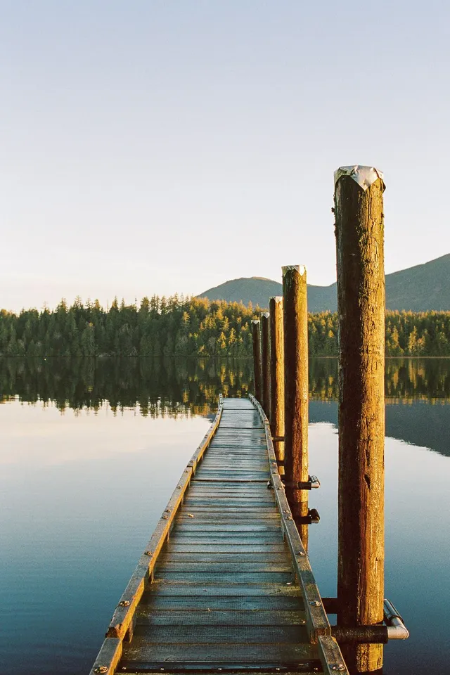 Wooden dock stretching into a still lake beneath forested hills