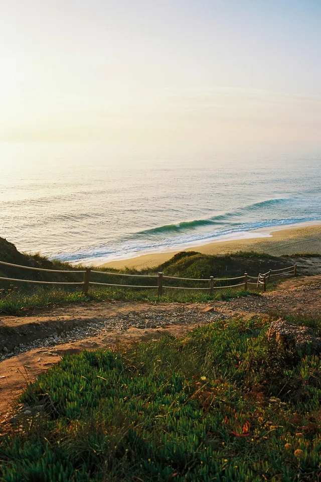 Clifftop path above a wide beach with long lines of surf