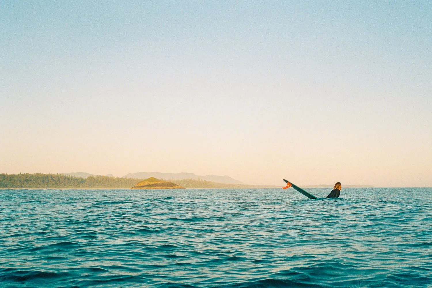 Surfer paddling on open water, coastline in the distance