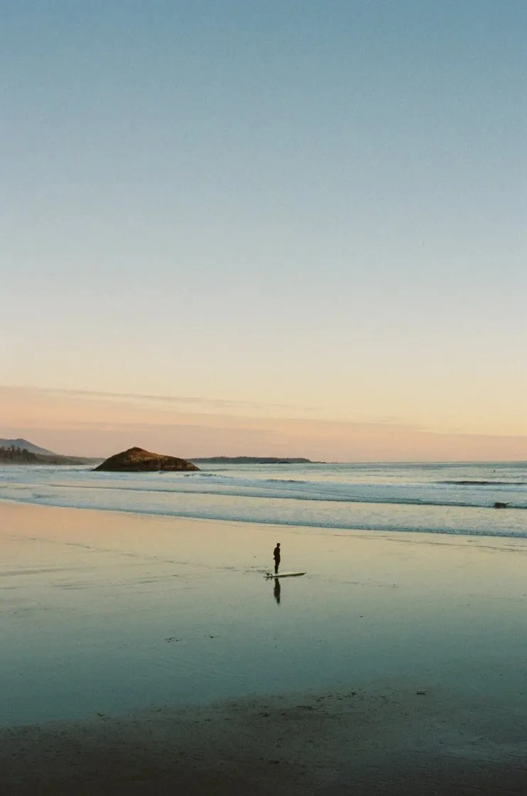 Lone surfer on a glassy beach at dusk